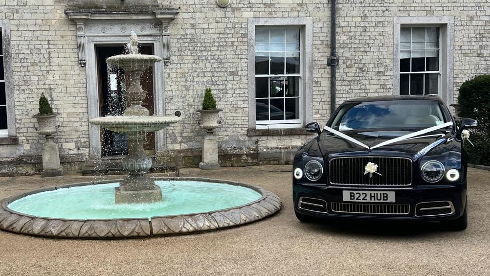 Dark Blue Bentley parked outside wedding venue with white ribbons and bows