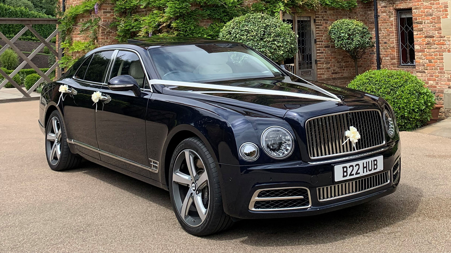 Blue Bentley Mulsanne dressed with white ribbons and bows on front grill and door handles parked in front of a wedding venue