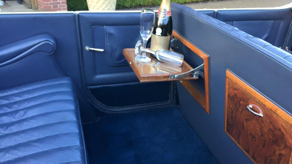 Vintage Rolls-Royce with a blue interior, wooden picnic table and a bottle of champagne and glassed standing on one of the picnic table