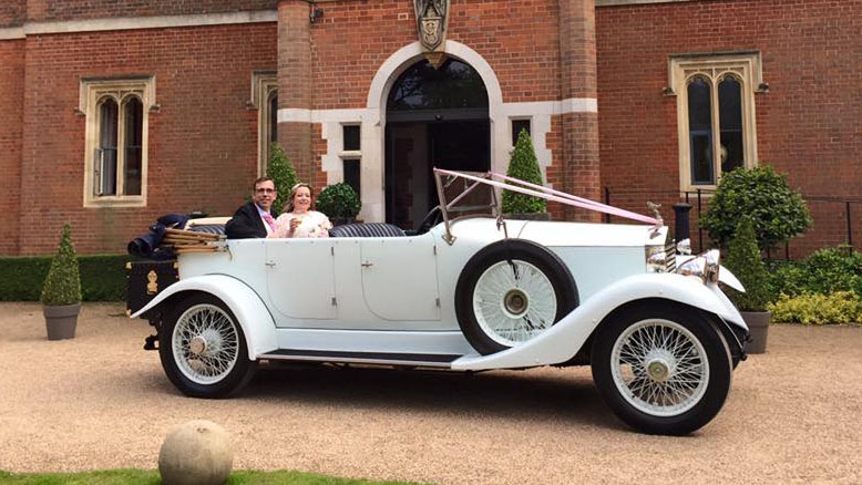 Right side view of a white vintgae rolls-royce parked in front of a wedding venue with Bride and Groom seating inside