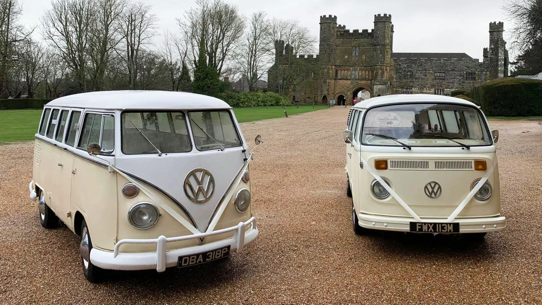 Two matching Classic VW Campervans in White and Ivory decorated with Ivory ribbons parked side-by-side. The left camper is the split screen version and the second campervan is a bay window.