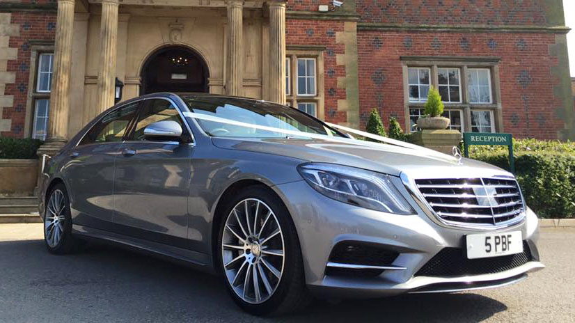 Front right view of Silver Mercedes decorated with white wedding ribbons parked in front of venue