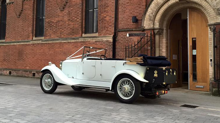 Left rear view of a white vintage Rolls-Royce with convertible roof fully open and black picnic trunk at the rear