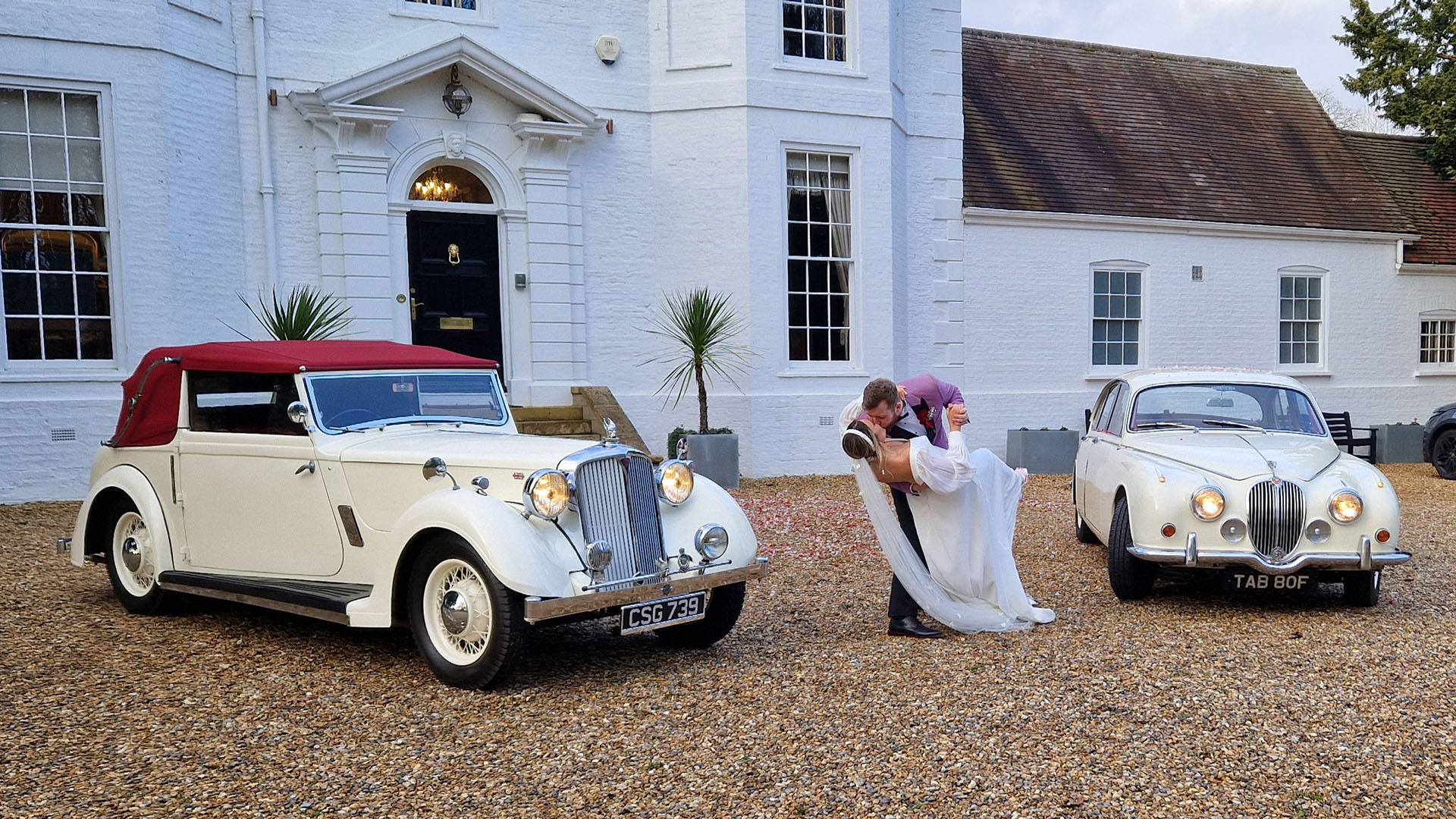 Vintage Rover Tickford with a Jaguar Mk2 at Barrington Hall wedding venue with bride and groom kissing in the middle both vehicles