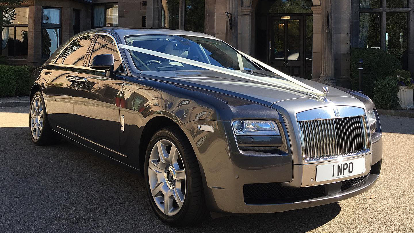 two tone silver Rolls-Royce Ghost with white wedding ribbons on its front bonnet