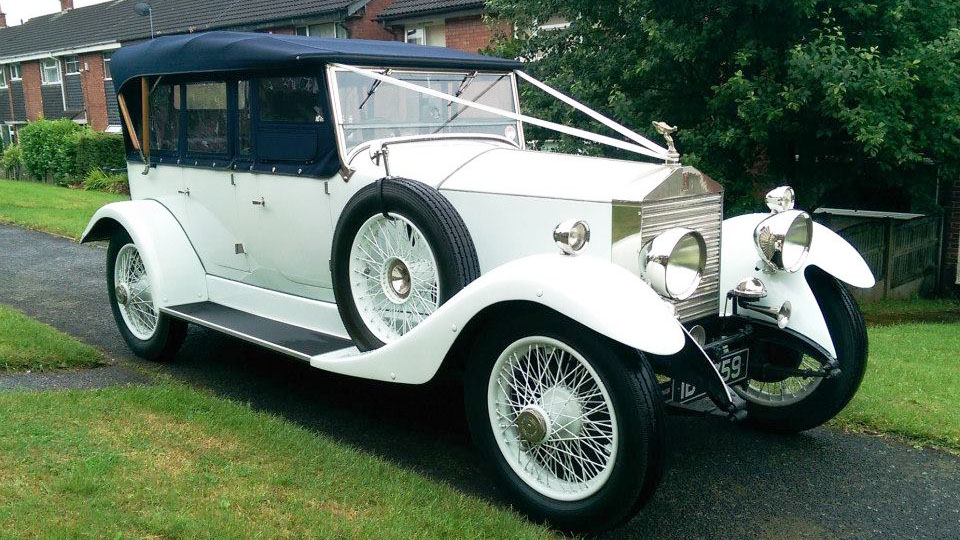 Vintage white Rolls-Royce with black soft-top convertible hood on and side windows.