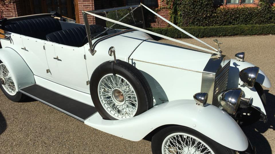 White vintage Rolls-Royce with spare wheel mounted on the side of the vehicle.