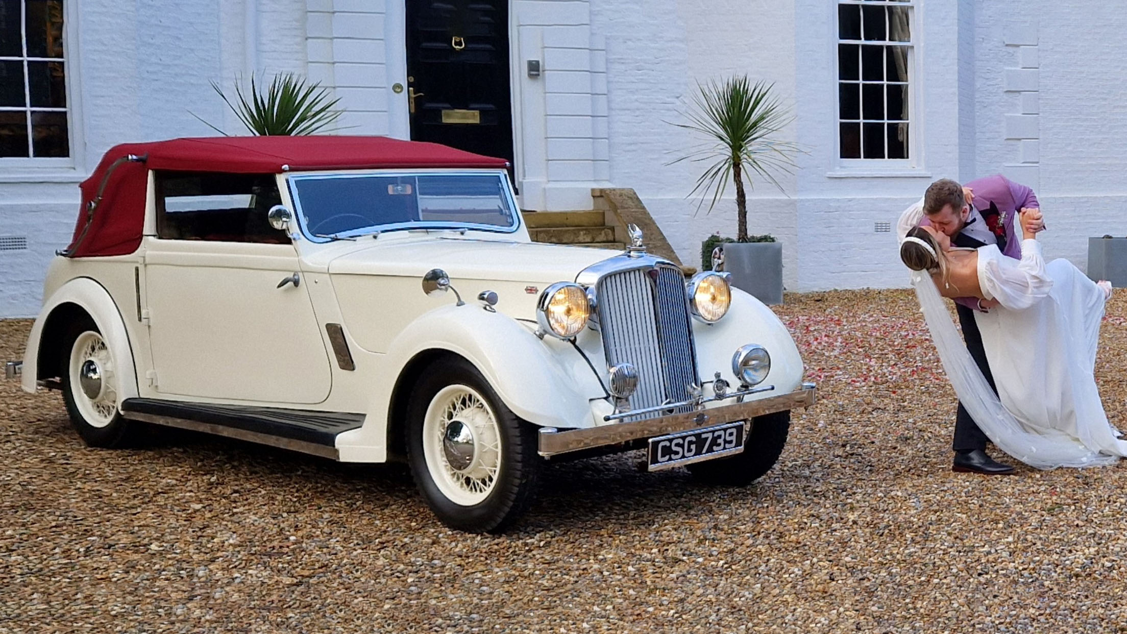 Ivory Vintage Tickford Wedding Car with burgundy convertible soft-top roof and Bride and Groom kissing on the side of the vehicle