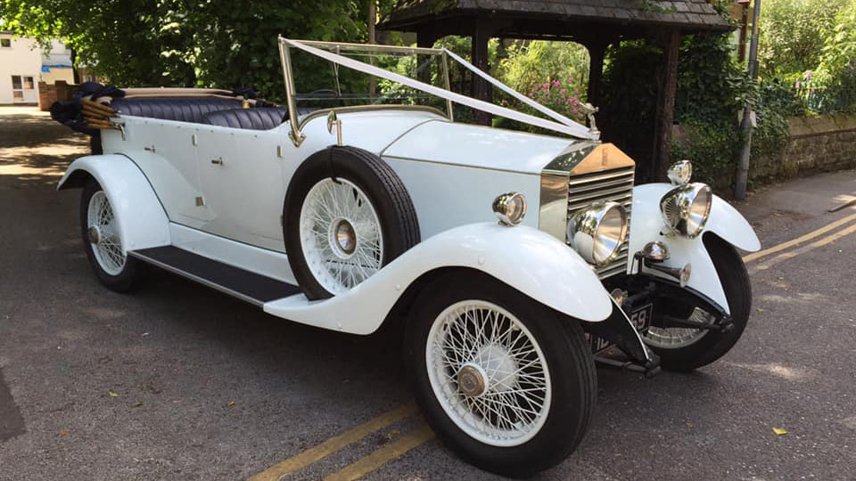 White vintage fully-convertible Rolls-Royce dressed with white wedding ribbons in front of a church entrance