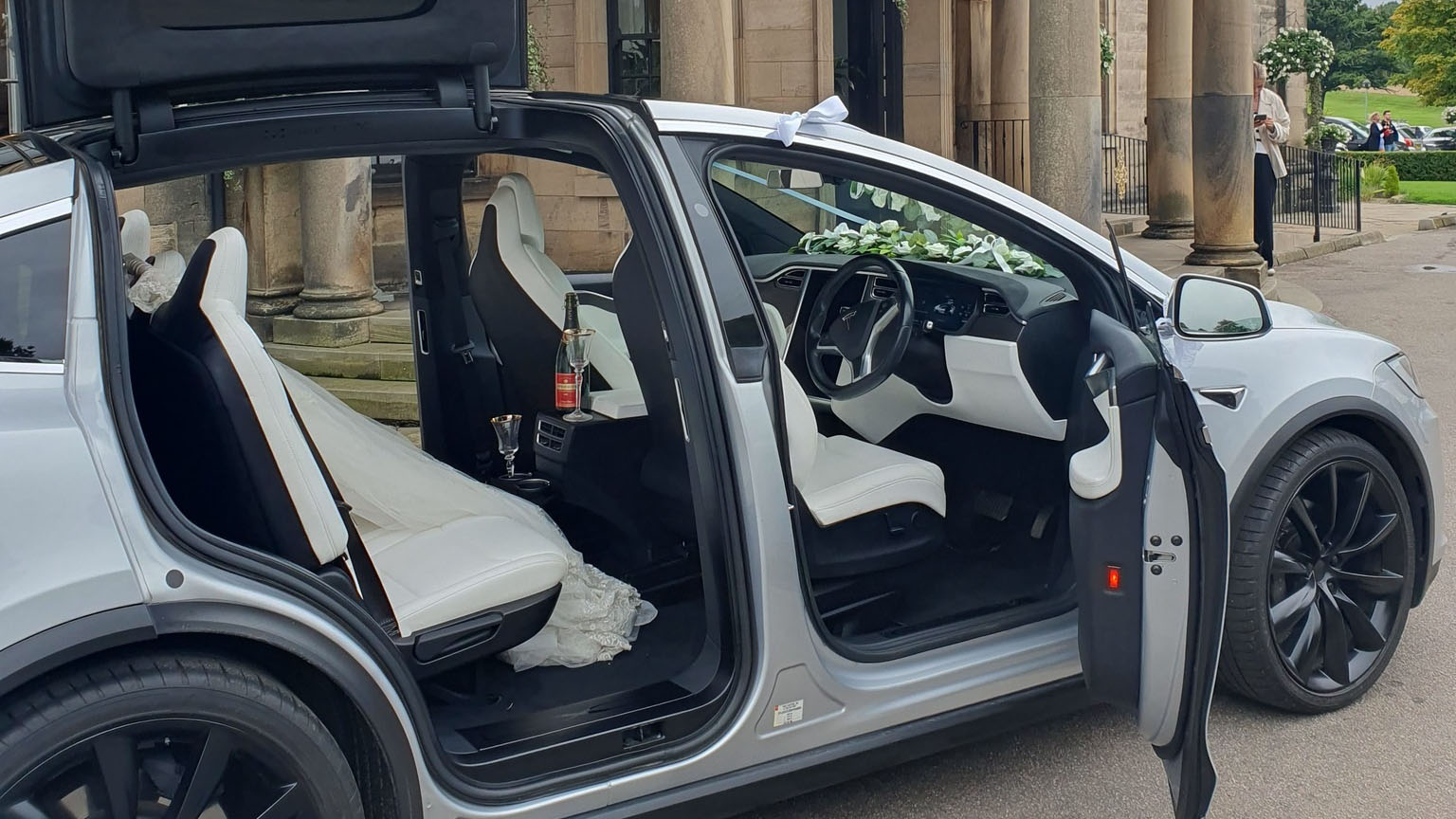 Right side view os a silver tesla X with all doors open showing a cream interior