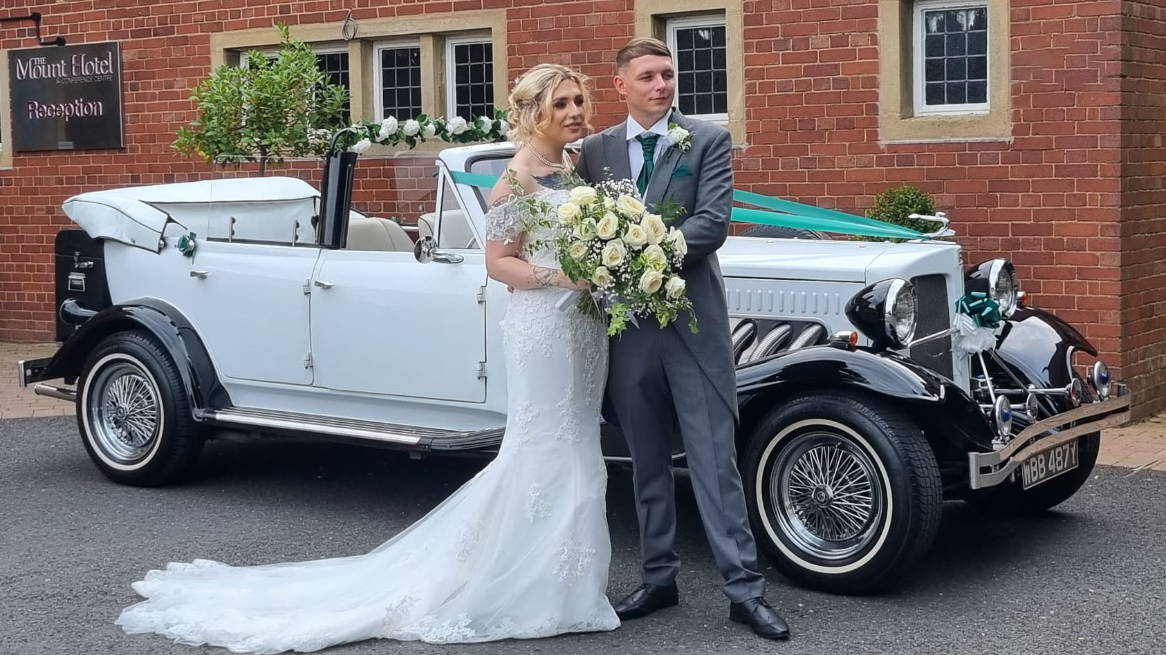 Bride and Groom standing in front of a convertible white Beauford