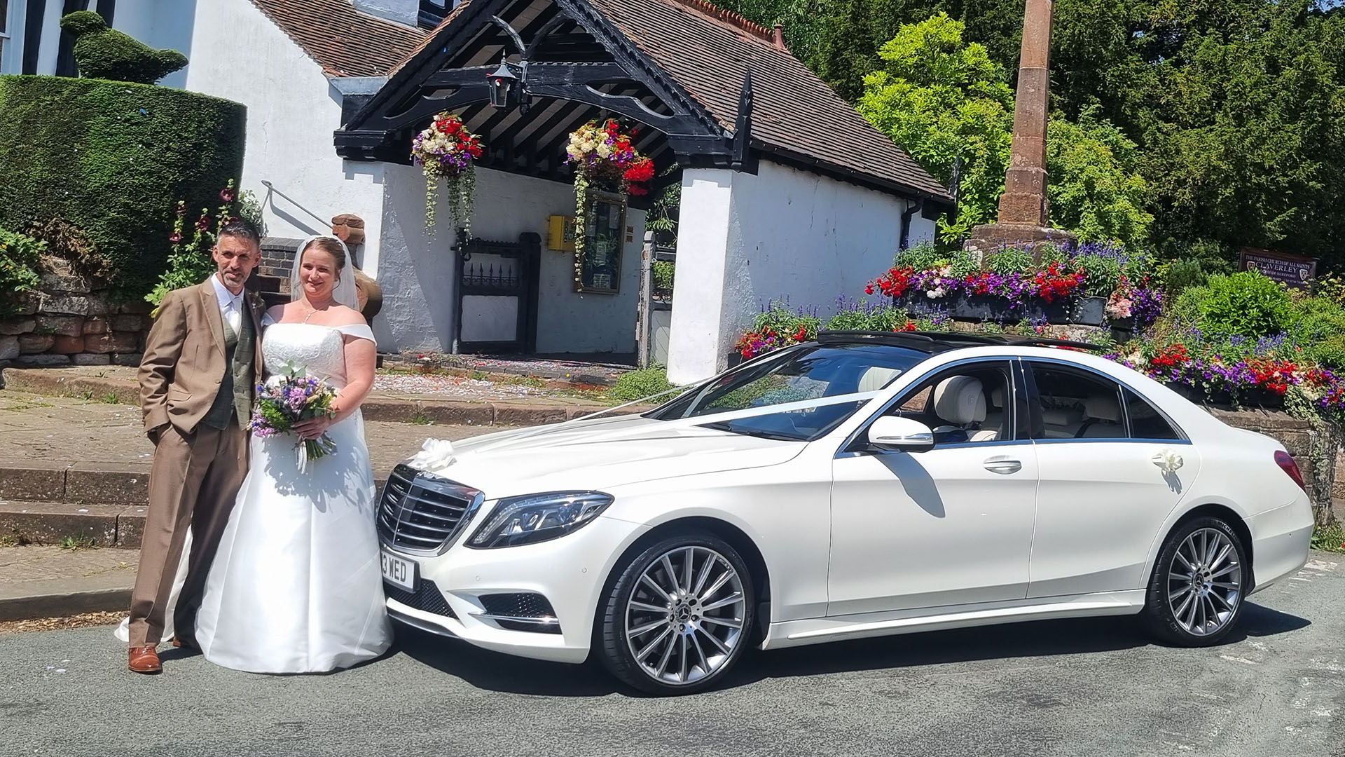 Bride and Groom standing in front of a white Mercedes S-class decorated with white ribbons