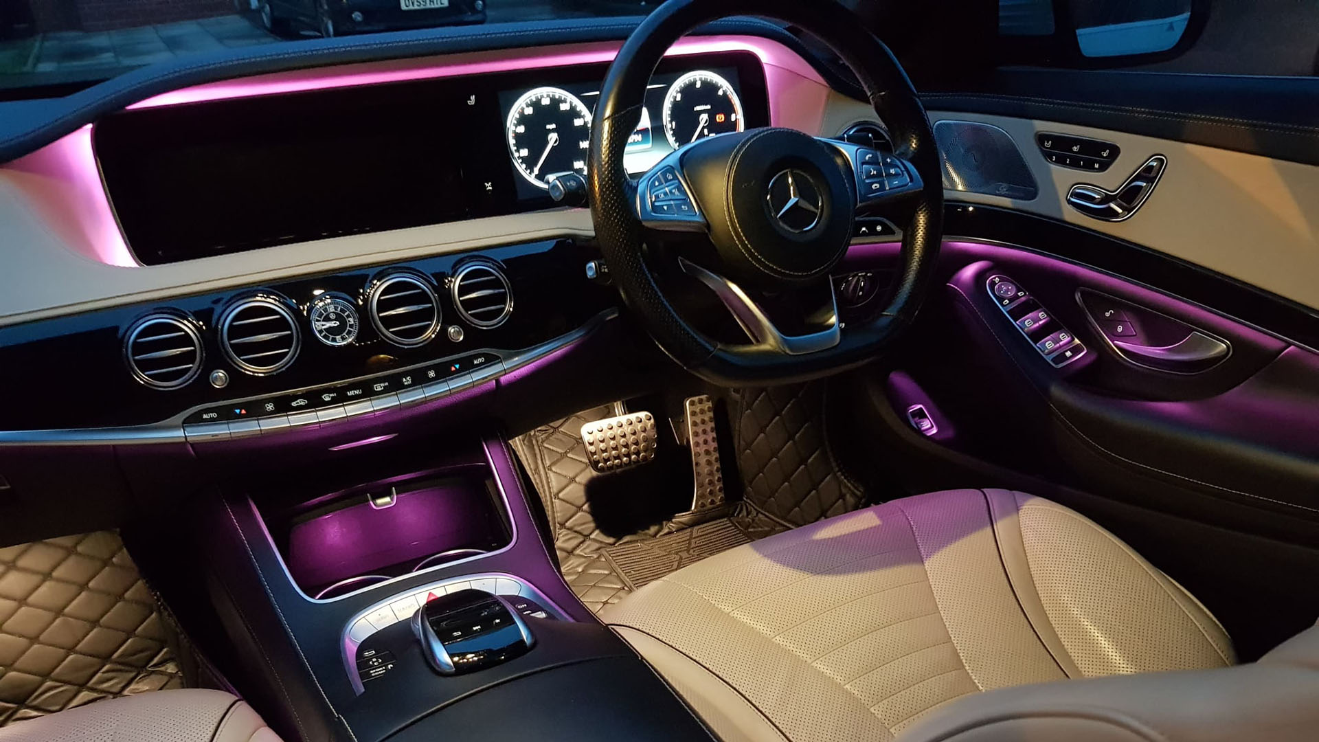 Front interior driver dashboard with cream seats and pink illuminated led lights