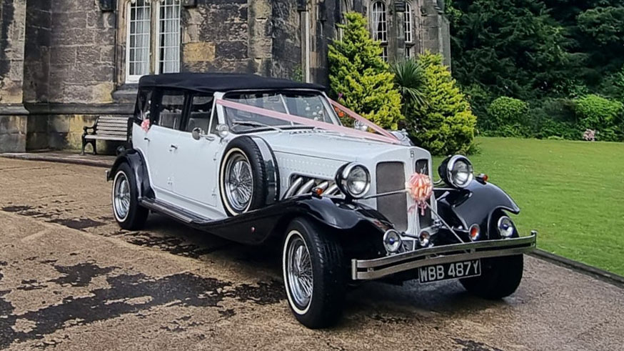 Black and White Beauford with black soft top roof closed and dressed with pale salmon wedding ribbons