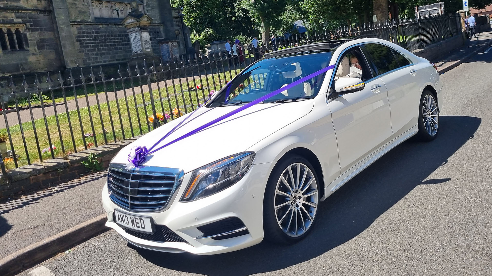 White Mercedes S-class with chrome alloy wheels and rear passengers privacy windows dressed with purple ribbons and bows.