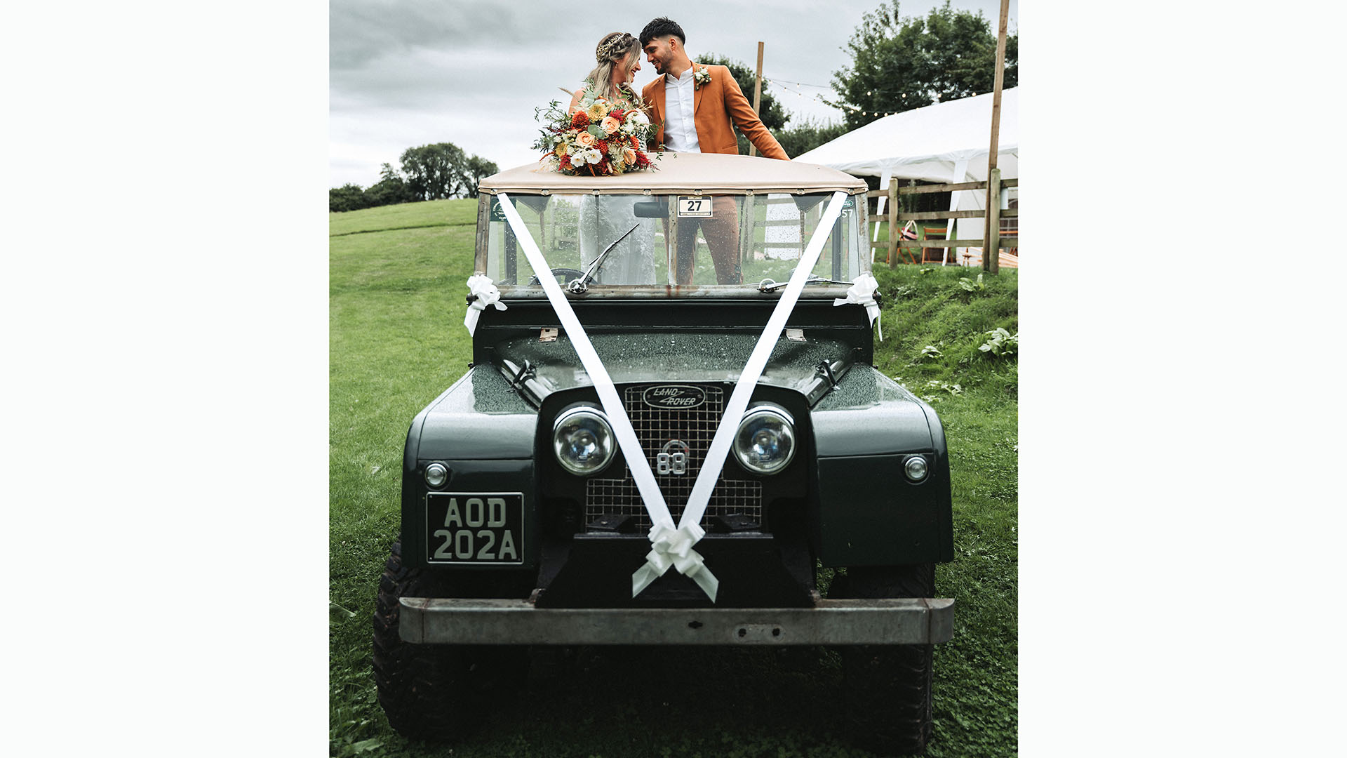 Bride and groom standing up in the rear of a green Land Rover