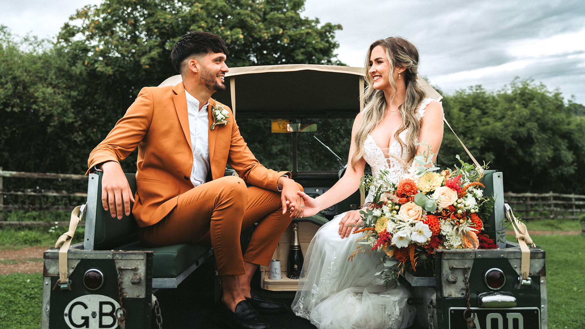 Bride and groom seating in the rear of a classic army green Land Rover