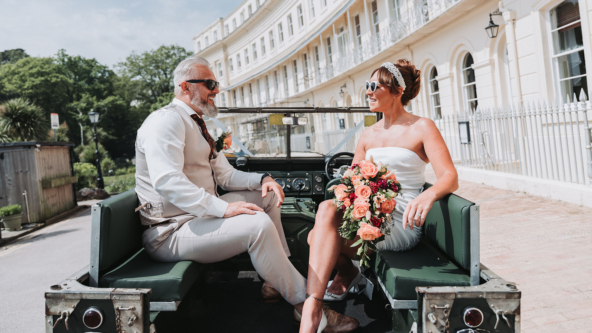 Bride and Groom seating in the rear of a Land Rover with canvas roof open in front of their wedding venue