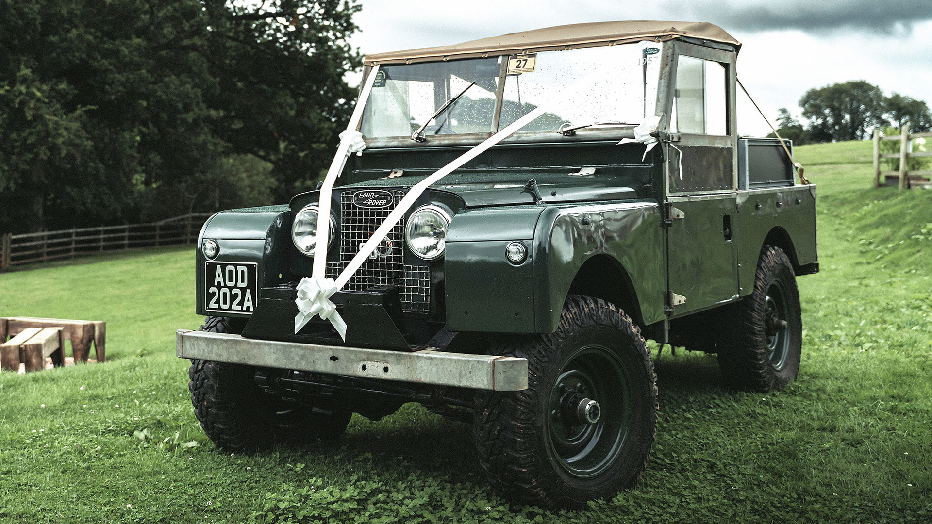 Classic Land Rover with white ribbons in a green field and soft top canvas roof open