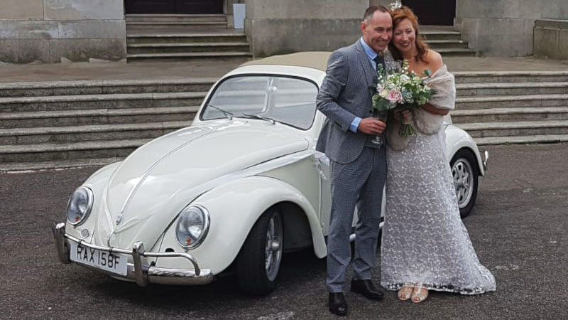 Classic Volkswagen Beetle with Bride and Groom standing in front of the vehicle