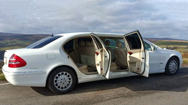 Rear view of White Stretched Mercedes Limousine with rear passengers doors open showing cream leater seats