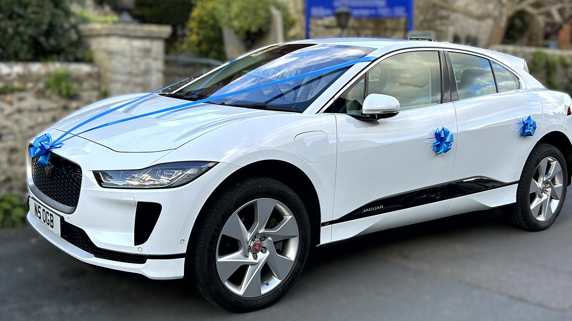 white Jaguar I-Pace parked in front of a church in Sussex decorated with Blue Ribbons and bows on the door handles