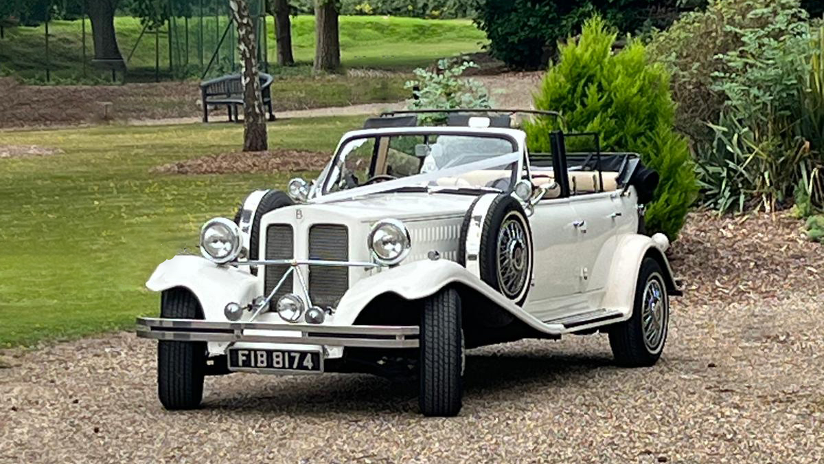 Vintage Beauford Wedding car entering wedding venue with white ribbons across its bonnet