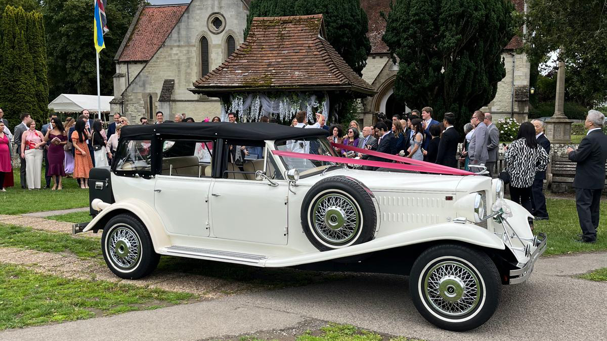 Beauford Convertible dressed with red ribbons parked in front of a church with wedding guests in the background