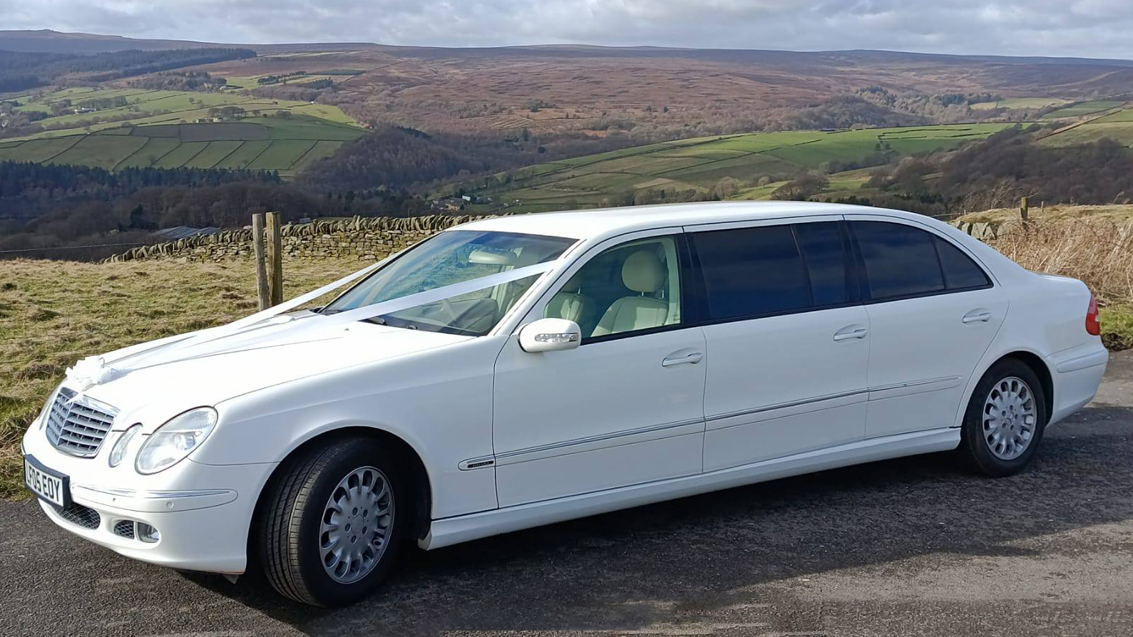 Left side view of White Stretched Mercedes Limousine dressed with white wedding ribbons across its front bonnet