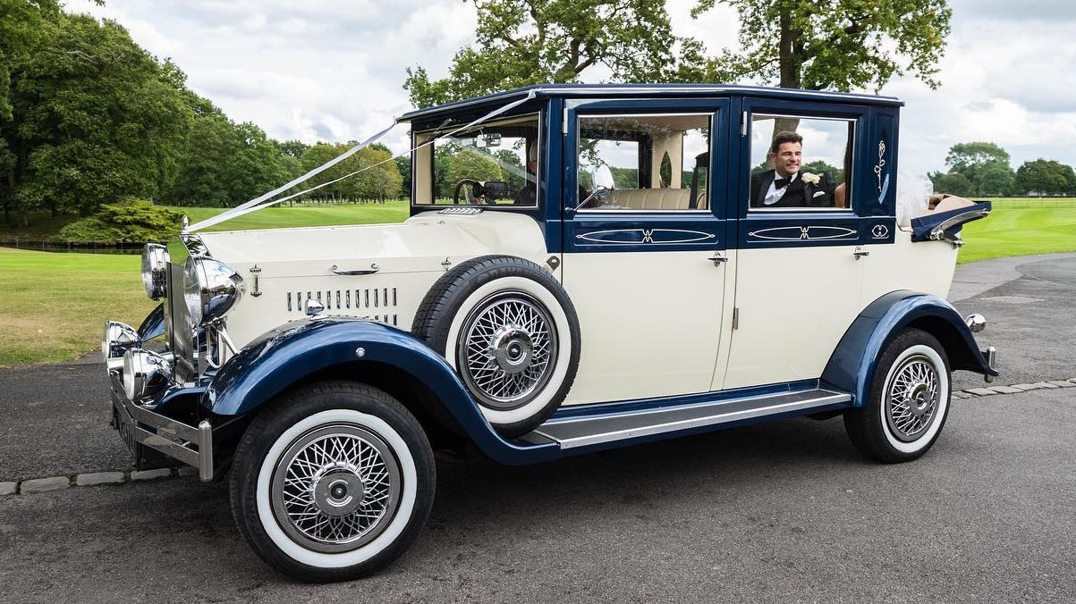 Vintage Imperial in Ivory and Blue with semi-convertible roof open and Bride and Groom seating in the back of the vehicle