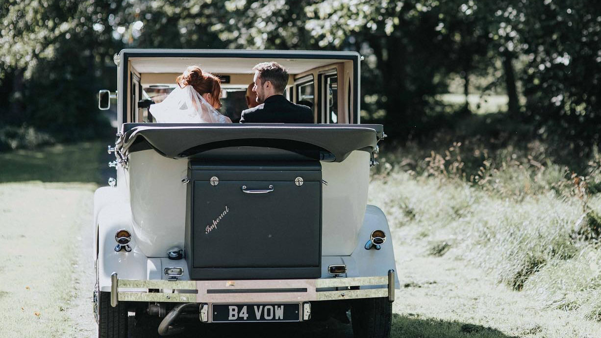 Bride and Groom seating inside a Vintage Imperial car with convertible rear soft top roof open