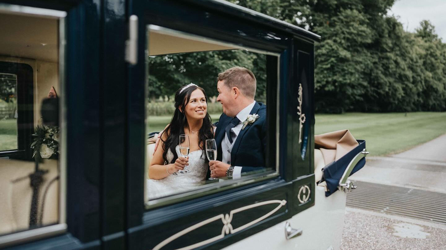 Bride and Groom seating inside an Imperial Car with rear semi-convertible roof open