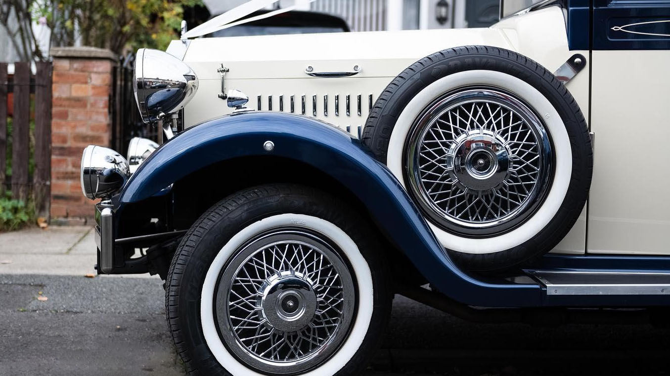 Close-up photo of front left wheel with white wall tires and chrome spoke wheels with view of the spare wheel mounted on the side of the vehicle