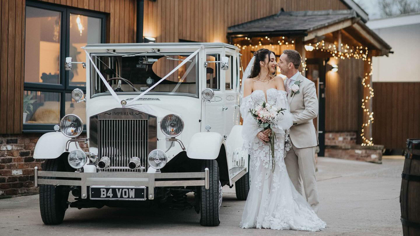 Bride and Groom holding each others standing next to a vintage Imperial car