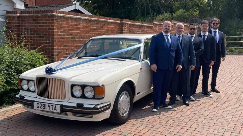 Groom and his Groomsmen standing in front of a  Ivory Bentley Turbo R dressed with blue ribbons and bows