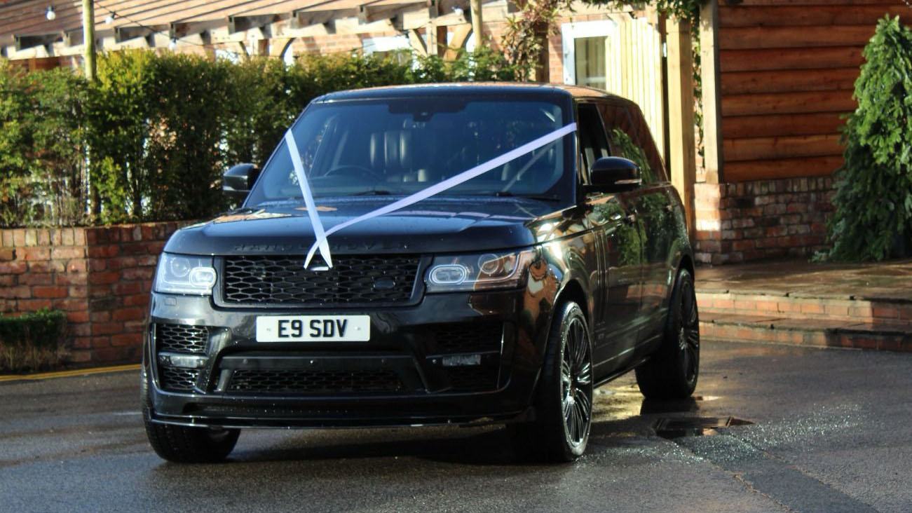 Front view of Black Range Rover with white wedding ribbons across its bonnet.