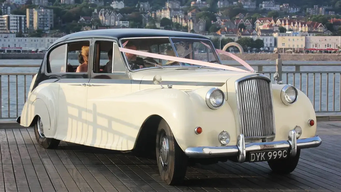 Ivory Austin Princess Limousine with black roof decorated with light pink ribbons across its bonnet