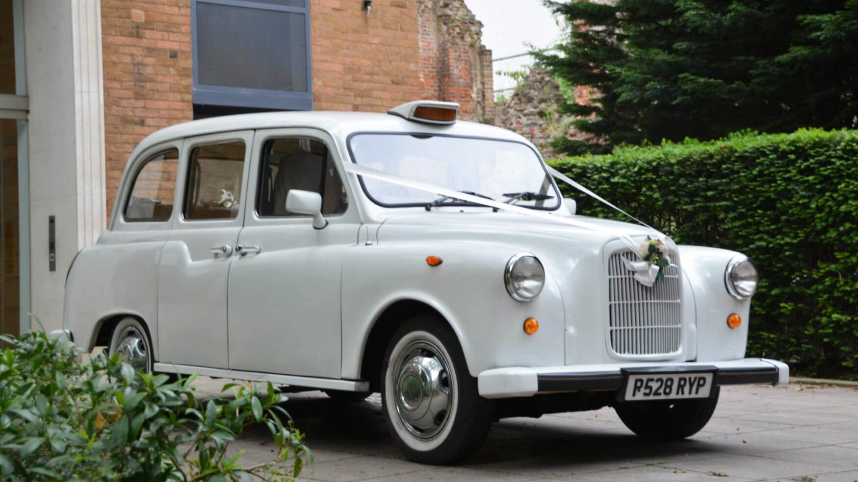 Classic white taxi cab with white wedding ribbons, white wall tires and taxi display sign on top