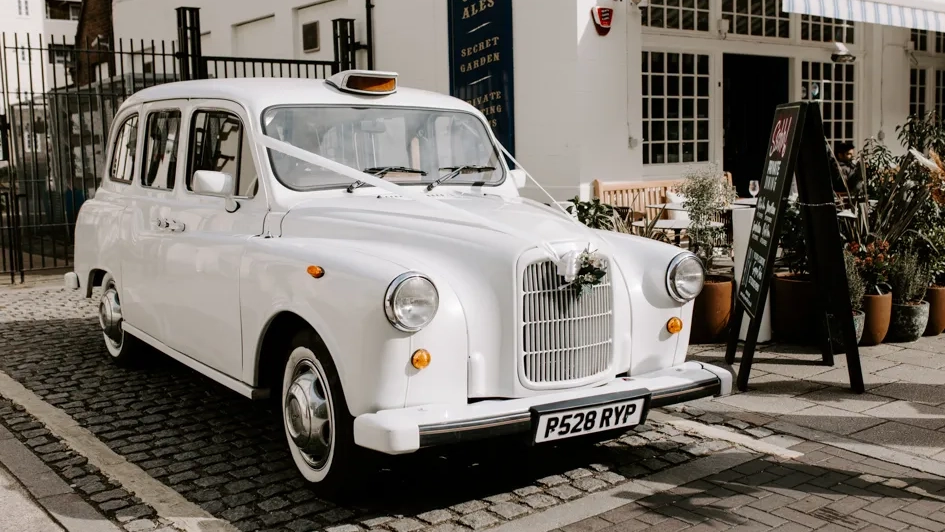 Classic white taxi cab with white wedding ribbons and flowers parked in the street of London