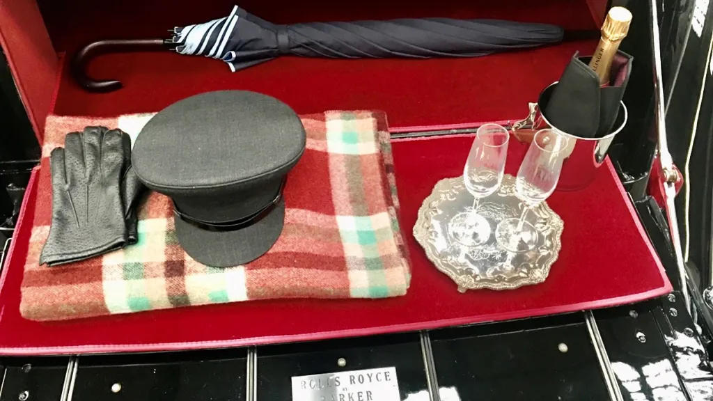 Opened rear boot of the vintage rolls-royce showing chauffeur's hat, umbrella, champagne glasses and bucket with a bottle inside.