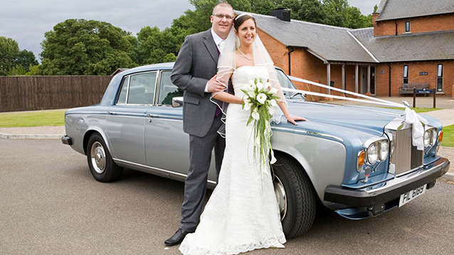 Rolls-Royce Silver Shadow II in light Blue and Silver decorated with white ribbons. Bride and Groom standing in front of the vehicle