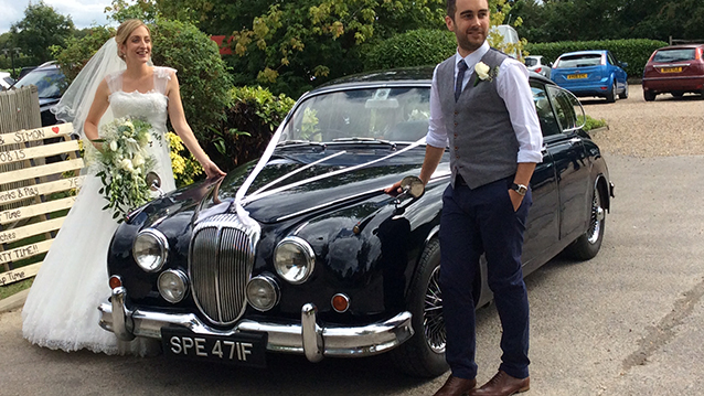 Bride and Groom standing on either side of a dark blue Daimler 250 V8