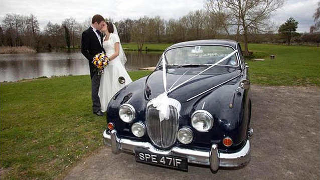 Bride and Groom kissing standing by classic Daimler