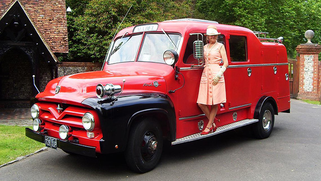 Unusual Wedding Car showing a vintage american Red Fire Truck with a lady wearing 50s cloth standing by the vehicle.