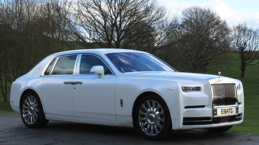 Luxurious Rolls-Royce Phantom 8 in white in a park with winter trees with no leaves.