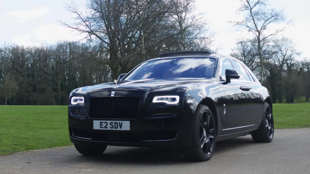 Front left view of Black Rolls-Royce Ghost with headlights switched parked in a park in London