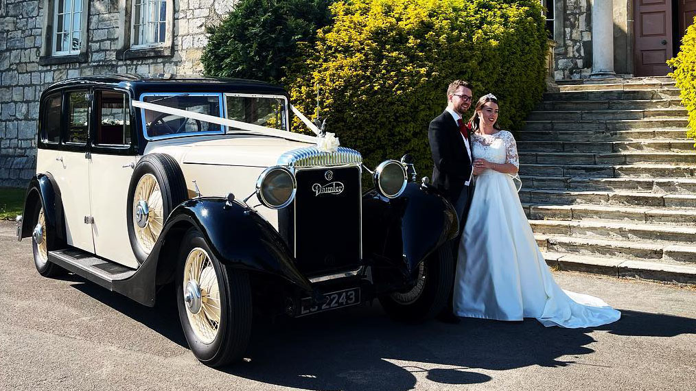 Feature photo showing bride and groom having photos outside their venue with their vintage car