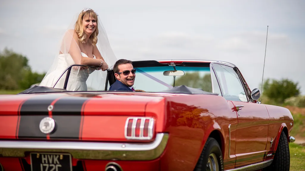 Bride and Groom seating inside the Ford Mustang looking back at their wedding photographer.