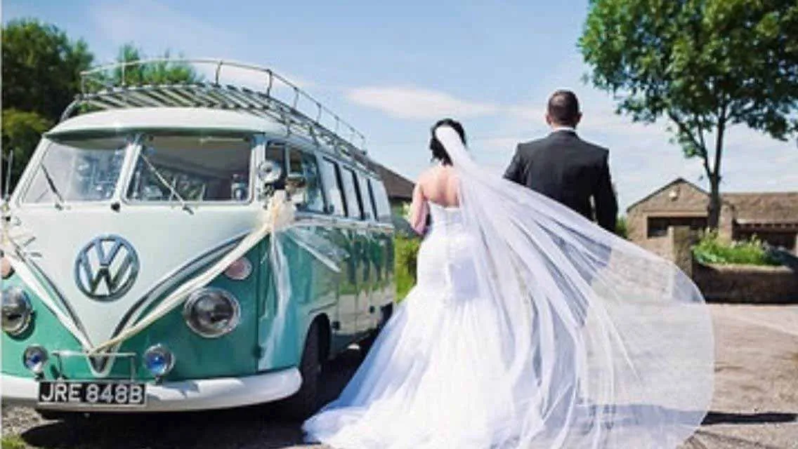 Retro Volkswagen Campervan decorated with white wedding ribbons. Bride and Groom next to the vehicle