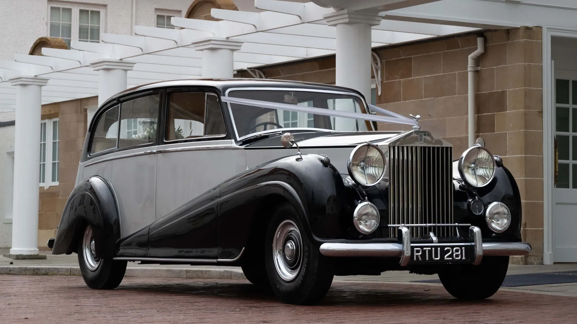 Rolls-Royce silver Wraith LWB with silver ribbons in front of wedding venue